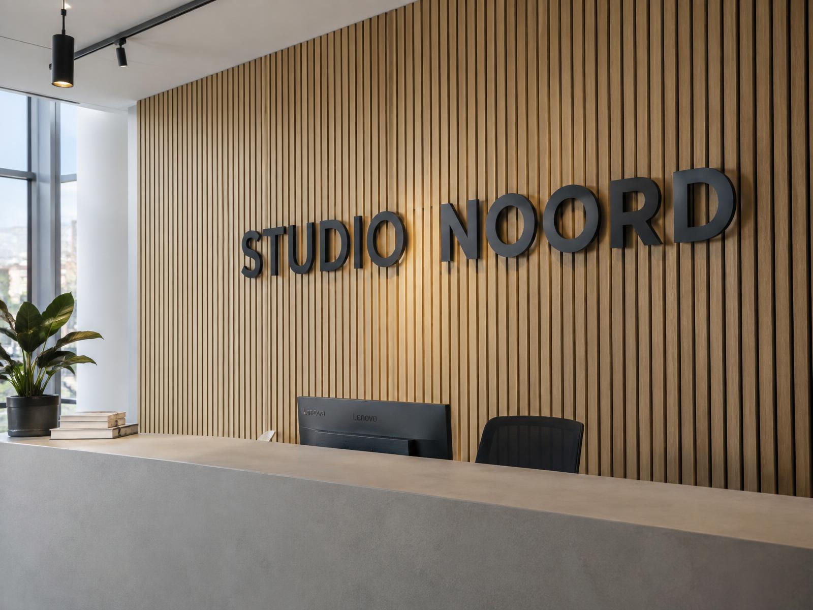 Grote mat zwarte 3D-letters 'Studio Noord' op een eiken lattenwand achter een receptiebalie